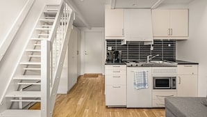 A modern kitchen with white cabinets, a microwave, a stove, and a sink. There is a staircase on the left and a door leading to another room. - Bryggen Suites - Perfect Location (Bergen)