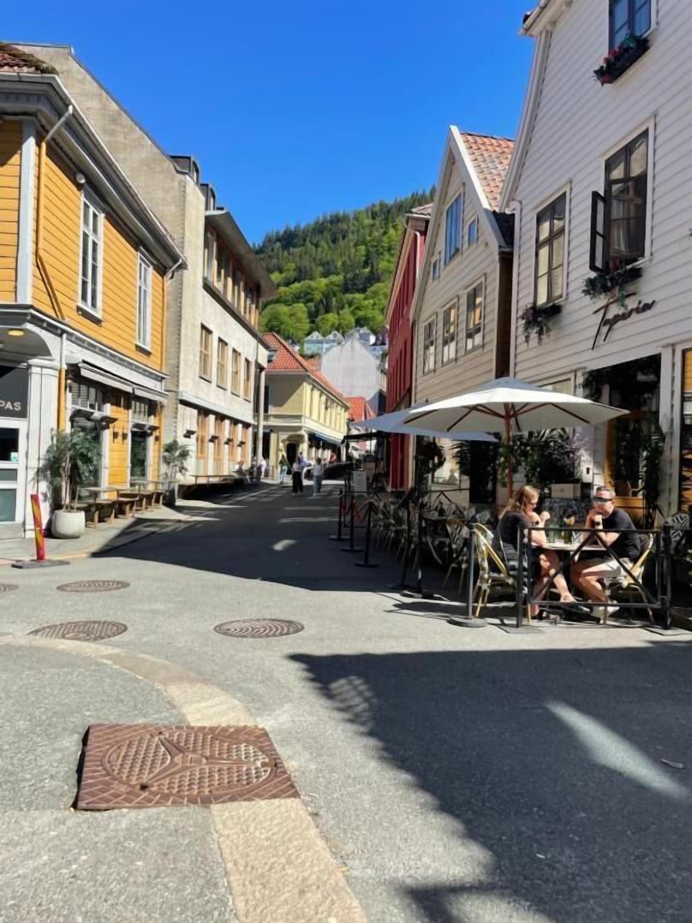 A street with buildings, outdoor seating, and a clear sky.