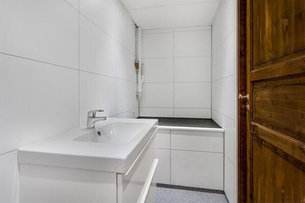 A small, clean bathroom with white tiles, a white sink, and a wooden door. - Bryggen Suites - Perfect Location (Bergen)
