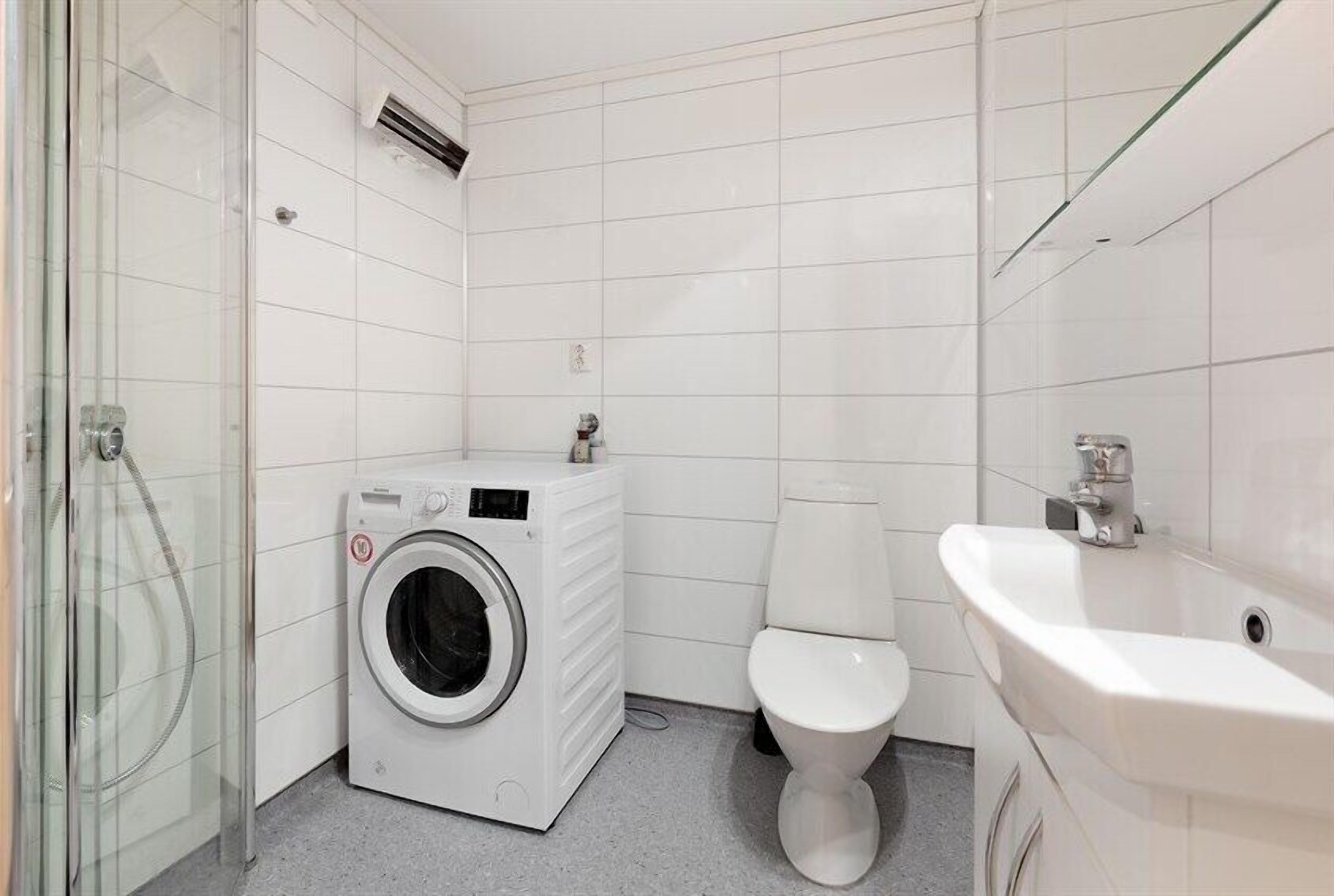 Een kleine, schone badkamer met witte tegels, een wasmachine, toilet en wastafel.
