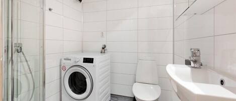 Een kleine, schone badkamer met witte tegels, een wasmachine, toilet en wastafel.