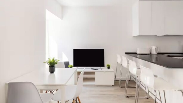 A modern, minimalist living space with a dining area, kitchen, and a flat-screen TV.