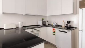 A modern kitchen with white cabinets, a black countertop, a microwave, a coffee maker, and a dishwasher.