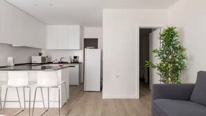 A modern kitchen with white cabinets, a dining area with two white chairs, and a grey sofa.