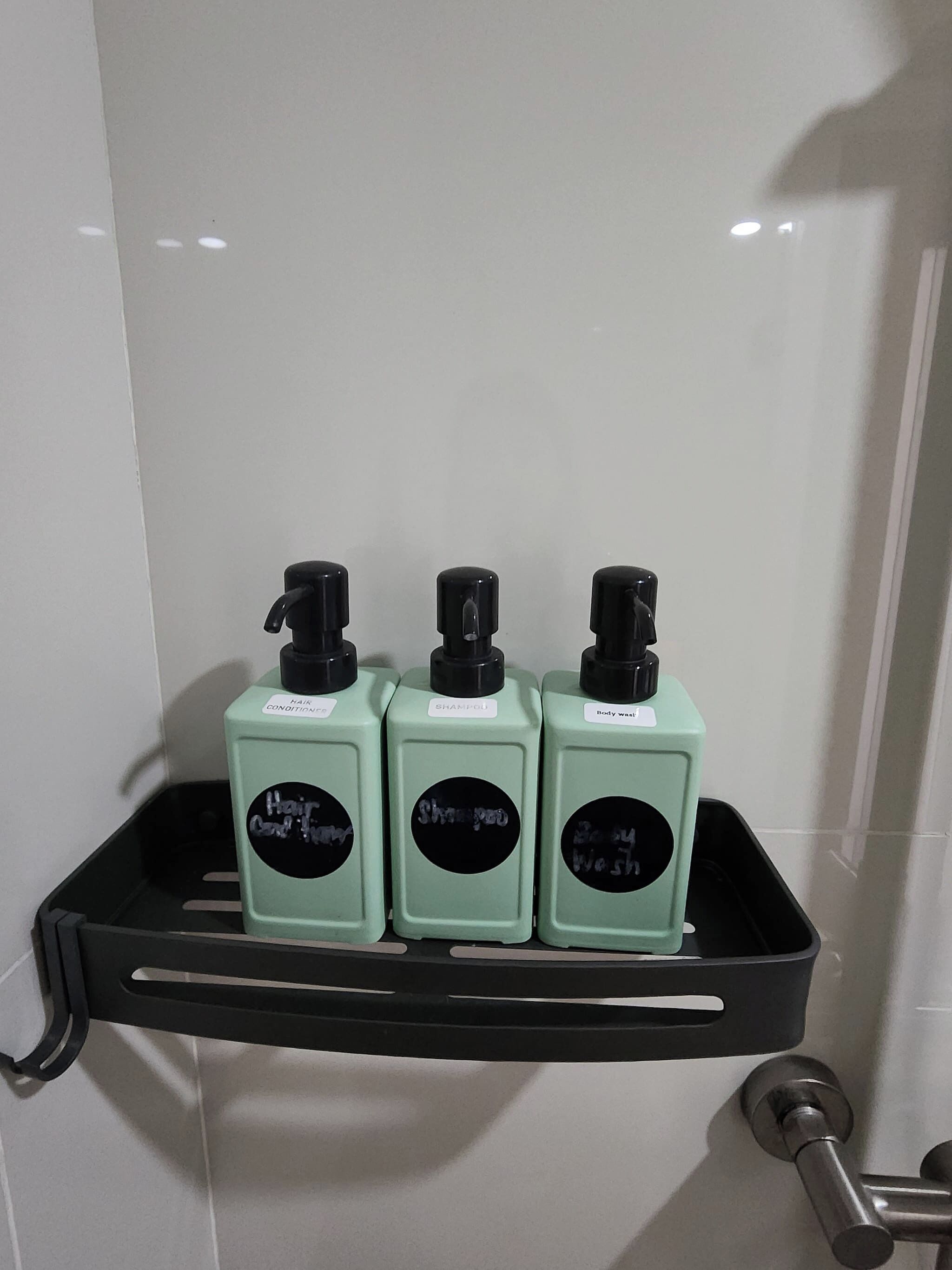 Une étagère de salle de bain avec trois flacons de produits pour les soins capillaires : après-shampoing, shampoing et gel douche.