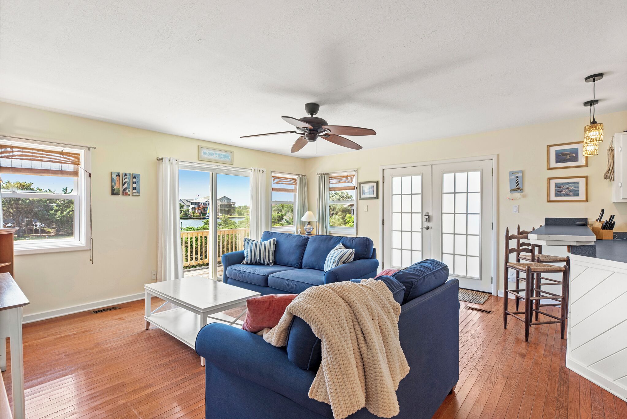 A spacious living room with a blue sofa, a ceiling fan, and a view of the outdoors through large sliding glass doors.