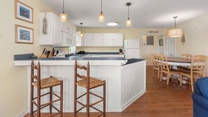 A kitchen with a central island, wooden chairs, and pendant lighting. - Surf'n Sound: Canalfront | Gas Grill (Avon)