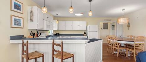 A kitchen with a central island, wooden chairs, and pendant lighting.