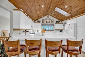 Une cuisine moderne dotée d’un îlot central, d’un plafond en bois et de meubles blancs.