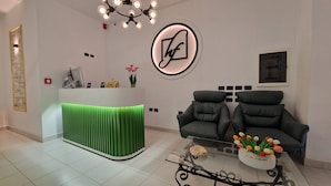 A reception area with a green reception desk, two black leather sofas, a glass coffee table with tulips, and a chandelier. - Frekel Hotel (Tirana)
