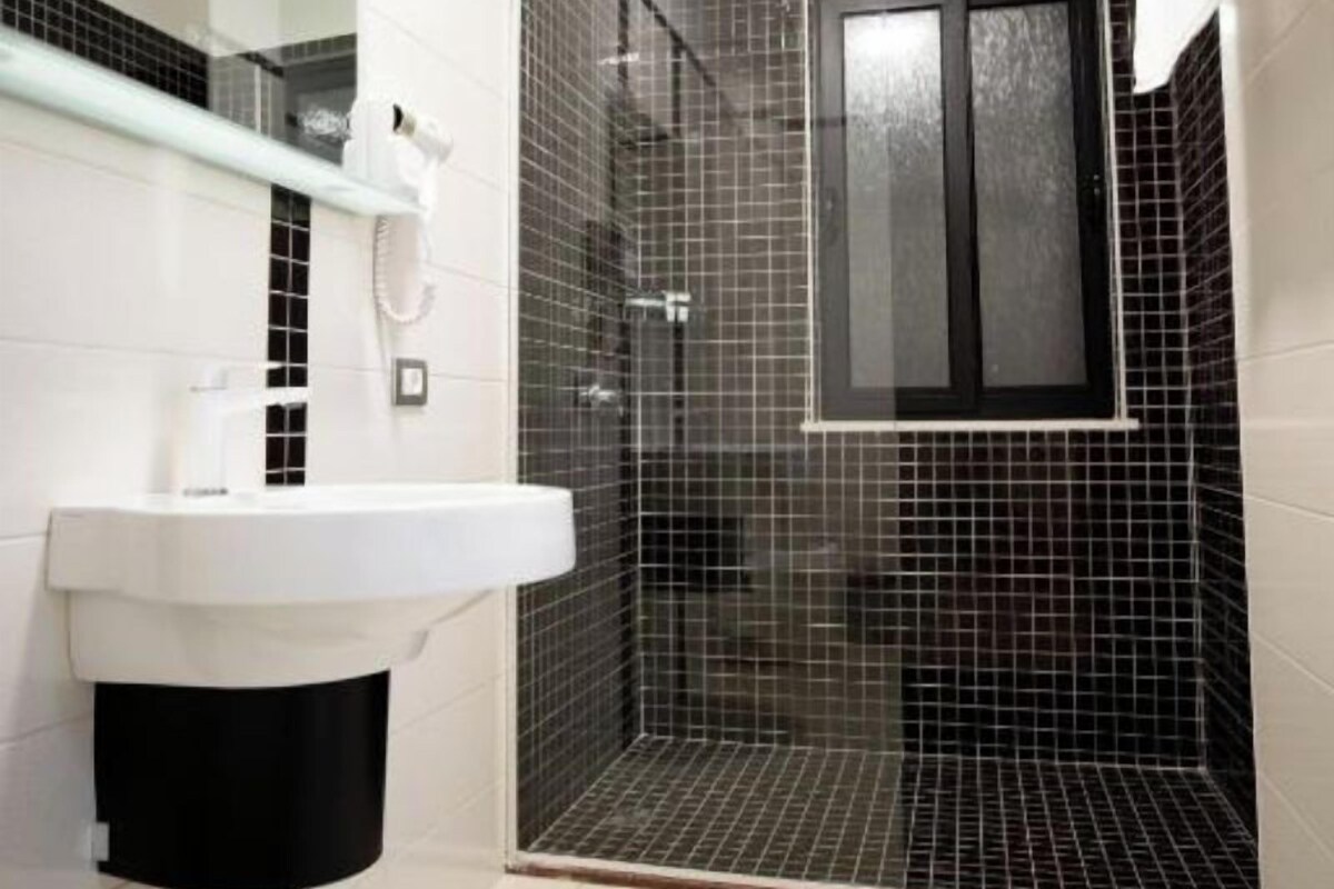 A bathroom with a white sink, a glass-enclosed shower, and a black tiled wall.