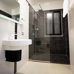 A bathroom with a white sink, a glass-enclosed shower, and a black tiled wall.