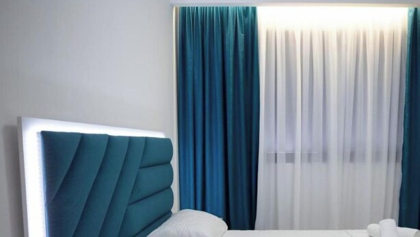 A hotel room with a bed, a nightstand, a remote control, and curtains. - Frekel Hotel (Tirana)