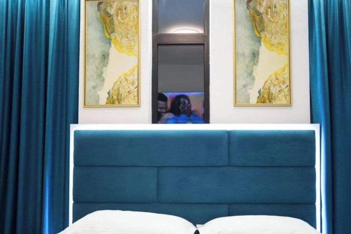 A bedroom with a large bed, blue curtains, and two framed paintings on the wall.