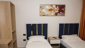 A hotel room with a single bed, a nightstand, a wardrobe, and a painting on the wall. - Frekel Hotel (Tirana)