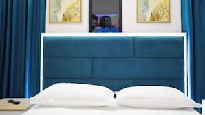 A bedroom with a large bed, blue curtains, and two framed paintings on the wall. - Frekel Hotel (Tirana)