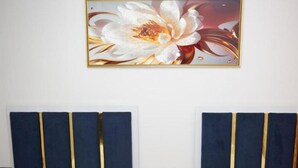 A hotel room with two beds, each with a blue headboard and white bedding. There is a wooden nightstand between the beds with a remote control on it. Above the beds, there is a framed floral artwork on the wall. - Frekel Hotel (Tirana)