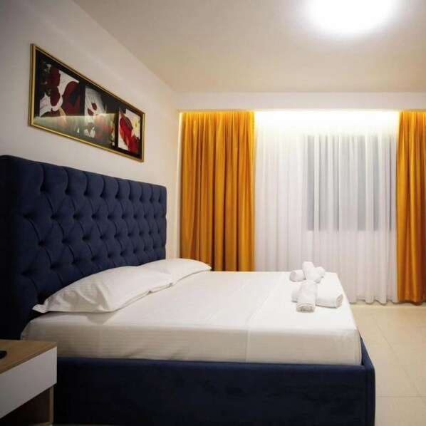 Une chambre d’hôtel avec un grand lit, une tête de lit, un tableau au mur et des rideaux.