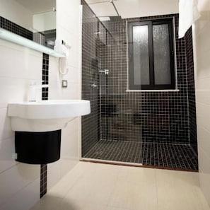 A bathroom with a white sink, a glass-enclosed shower, and a black-tiled wall. - Frekel Hotel (Tirana)