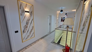A hallway with a glass railing, a fire extinguisher, and a framed artwork on the wall. - Frekel Hotel (Tirana)