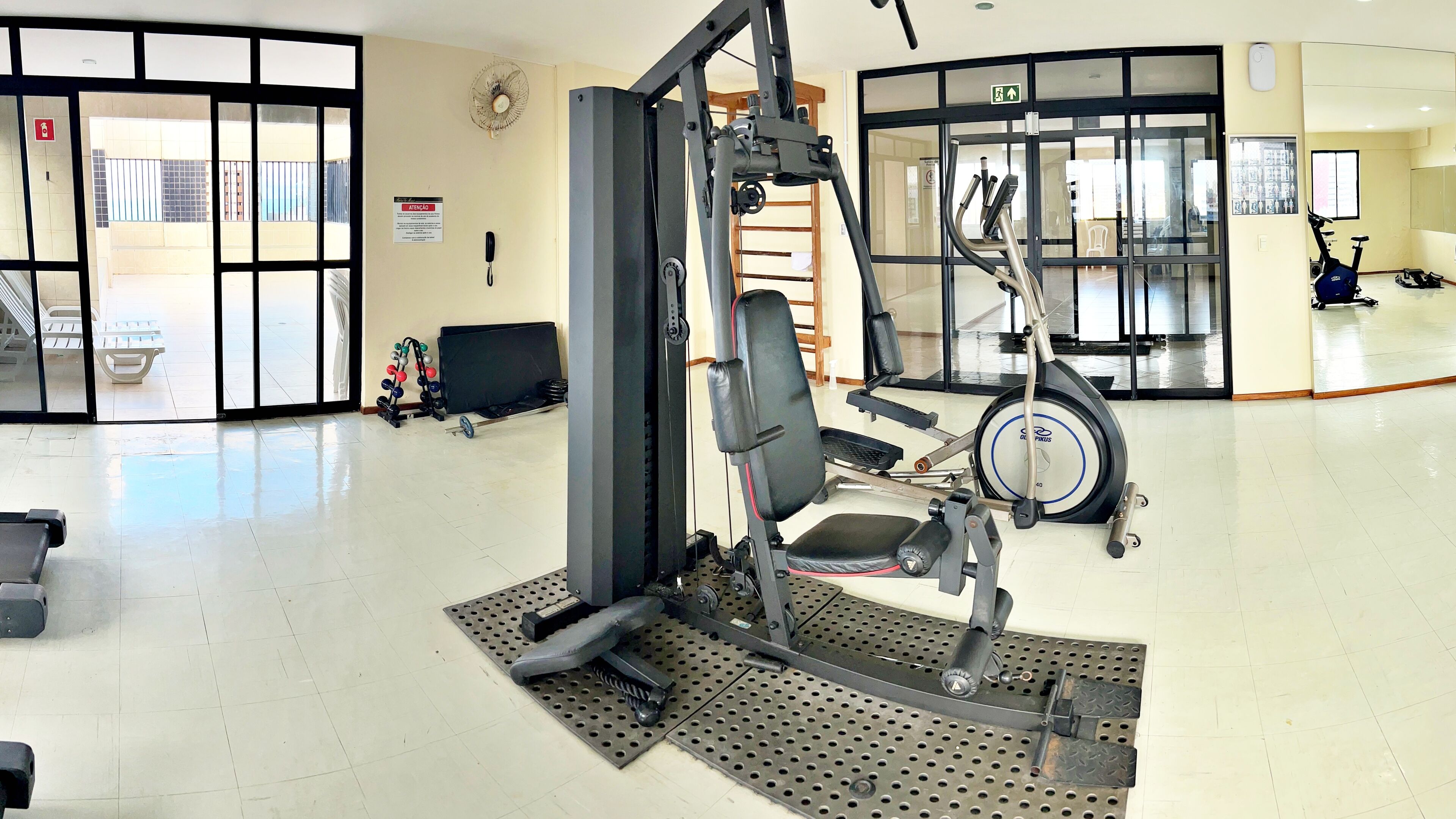 A gym with exercise equipment, a fan, and a phone on the wall.