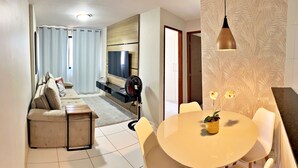 A modern living room with a sofa, TV, and a dining area with a table and chairs. - Vacation - edf. Barão de Mauá - 2 bedroom apt. 903, fully furnished in Jatiúca (Jatiúca Maceió)