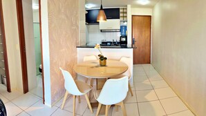 A dining area with a round table and four chairs, a vase with a flower, and a kitchen in the background. - Vacation - edf. Barão de Mauá - 2 bedroom apt. 903, fully furnished in Jatiúca (Jatiúca Maceió)