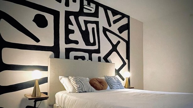 A modern bedroom with a large bed, white bedding, and a geometric wall design.