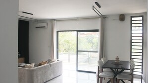 A modern living room with a sofa, a dining table with chairs, and a sliding glass door leading to an outdoor area.