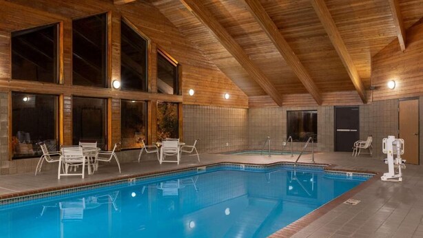 Una piscina interna con travi in legno, pareti piastrellate e poltrone relax.