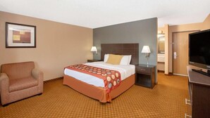 Una camera d'albergo con un letto, una sedia, una TV e un quadro appeso al muro.