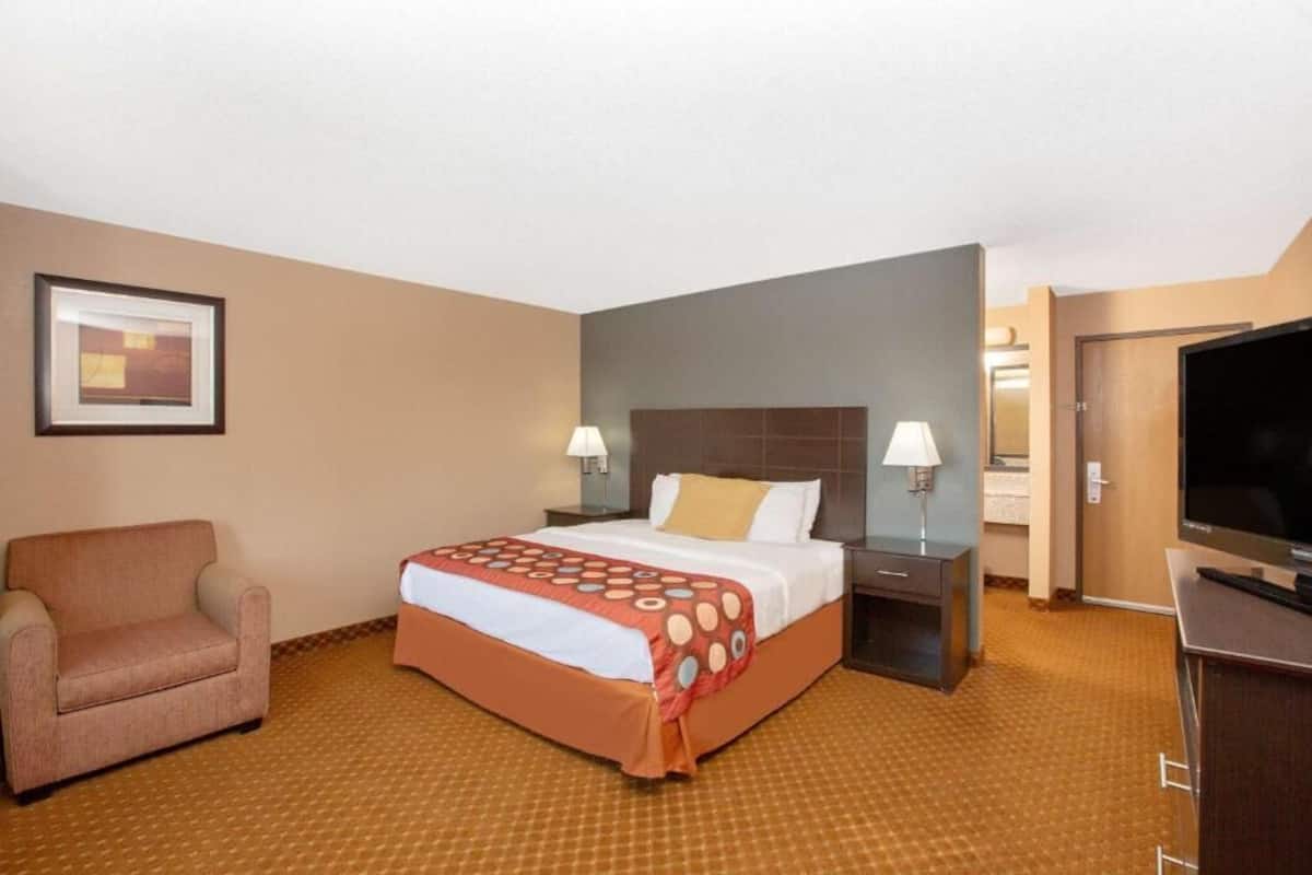 Ein Hotelzimmer mit einem Bett, einem Sessel, einem Fernseher und einem gerahmten Bild an der Wand.