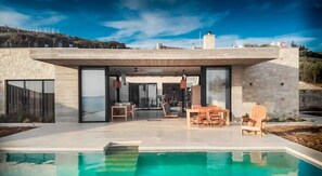 A modern house with a swimming pool, outdoor seating, and a view of the surrounding landscape. - Modern and stylish with sea view (crete)