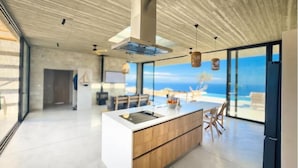 A modern kitchen with a large island, a dining area with chairs, and a view of the ocean. - Modern and stylish with sea view (crete)