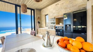 A modern kitchen with a view of the ocean, a metal bowl of oranges, and a stainless steel kettle on the counter. - Modern and stylish with sea view (crete)