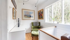A cozy room with a wooden floor, a green armchair with a striped pillow, a white radiator, and a window with a view of trees. - Elf House in Heart of Downtown Hafnarfjordur (Hafnarfjörður)