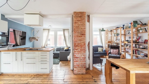 A spacious living area with a kitchen, a brick column, a wooden dining table, and a bookshelf filled with books. - Elf House in Heart of Downtown Hafnarfjordur (Hafnarfjörður)