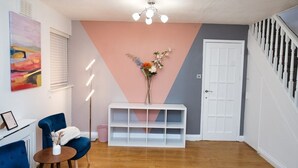 A modern interior with a blue armchair, a white console table with a vase, and a staircase. - Close to city centre home (Bradwell Common)