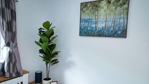 A room with a large painting of a forest, a potted plant, and a framed picture on a wooden shelf. - Close to city centre home (Bradwell Common)