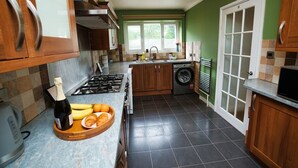 A modern kitchen with a gas stove, wooden cabinets, a built-in oven, a washing machine, and a large window providing natural light. - Close to city centre home (Bradwell Common)