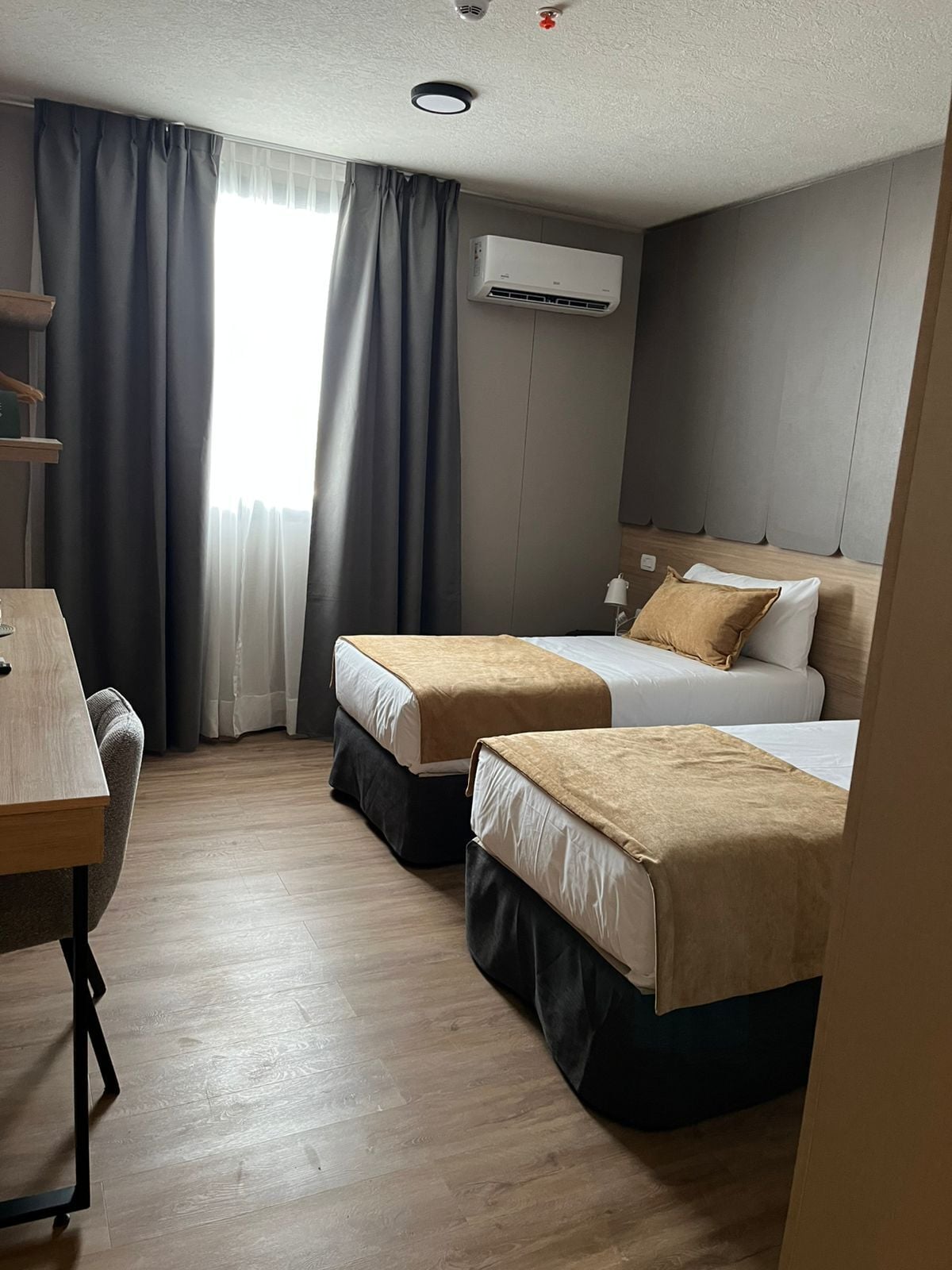 A hotel room with two beds, a desk, and a window with curtains.