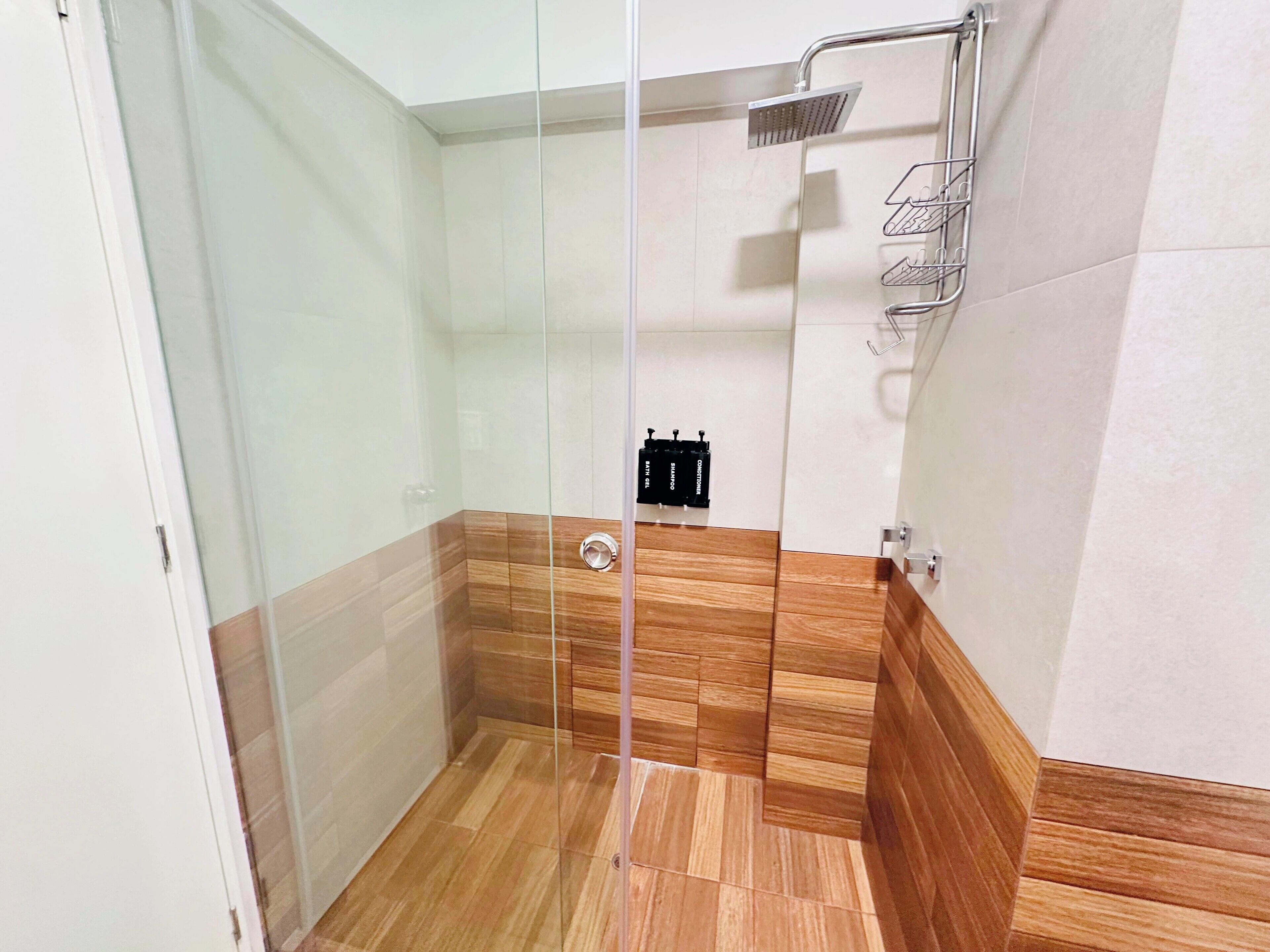 Una ducha con cerramiento de vidrio, un cabezal de ducha manual, un perchero y un panel de control en la pared.