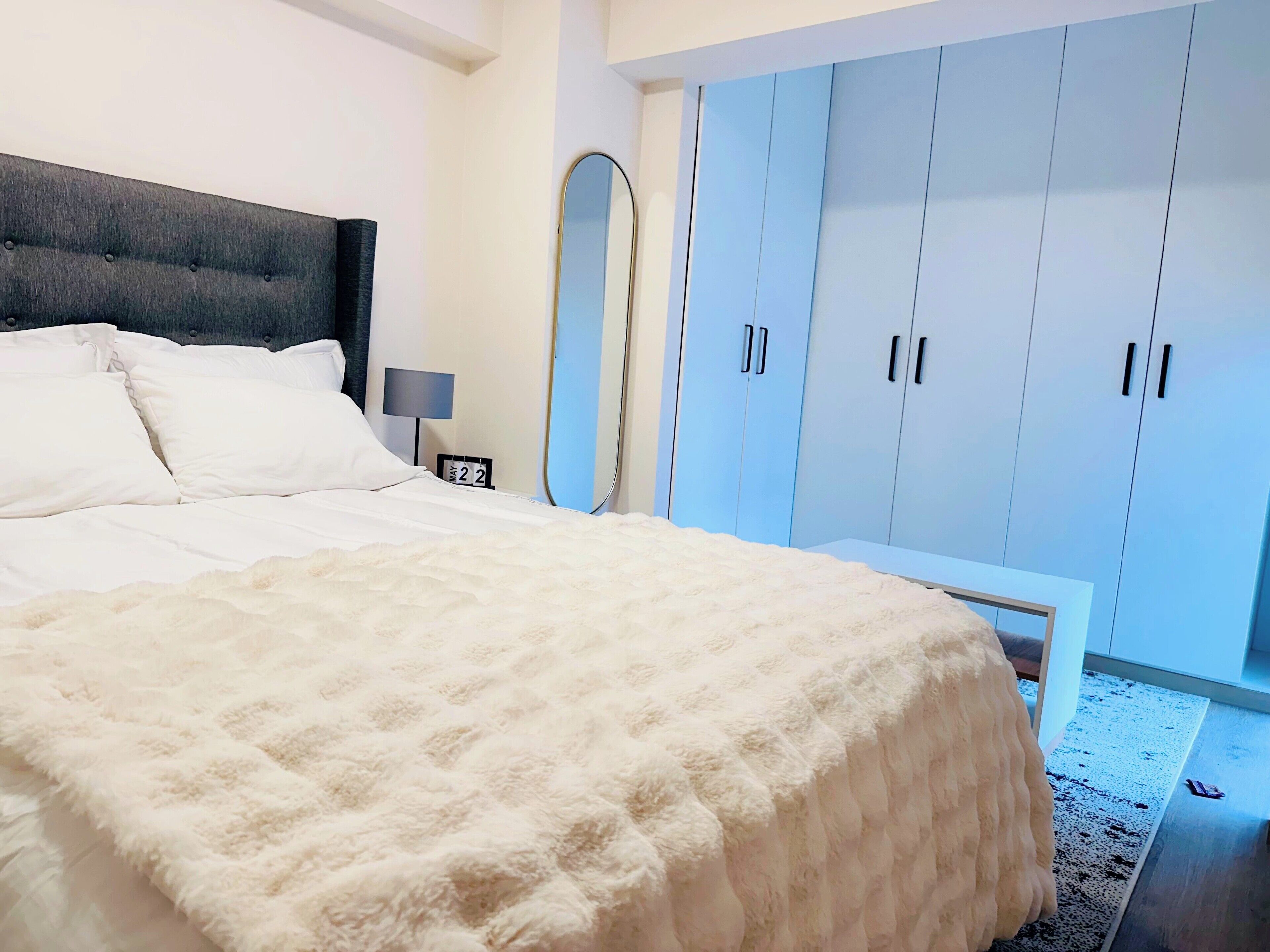 Ein Schlafzimmer mit einem großen Bett, einem Nachttisch, einem Spiegel und hellblauen Kleiderschränken.