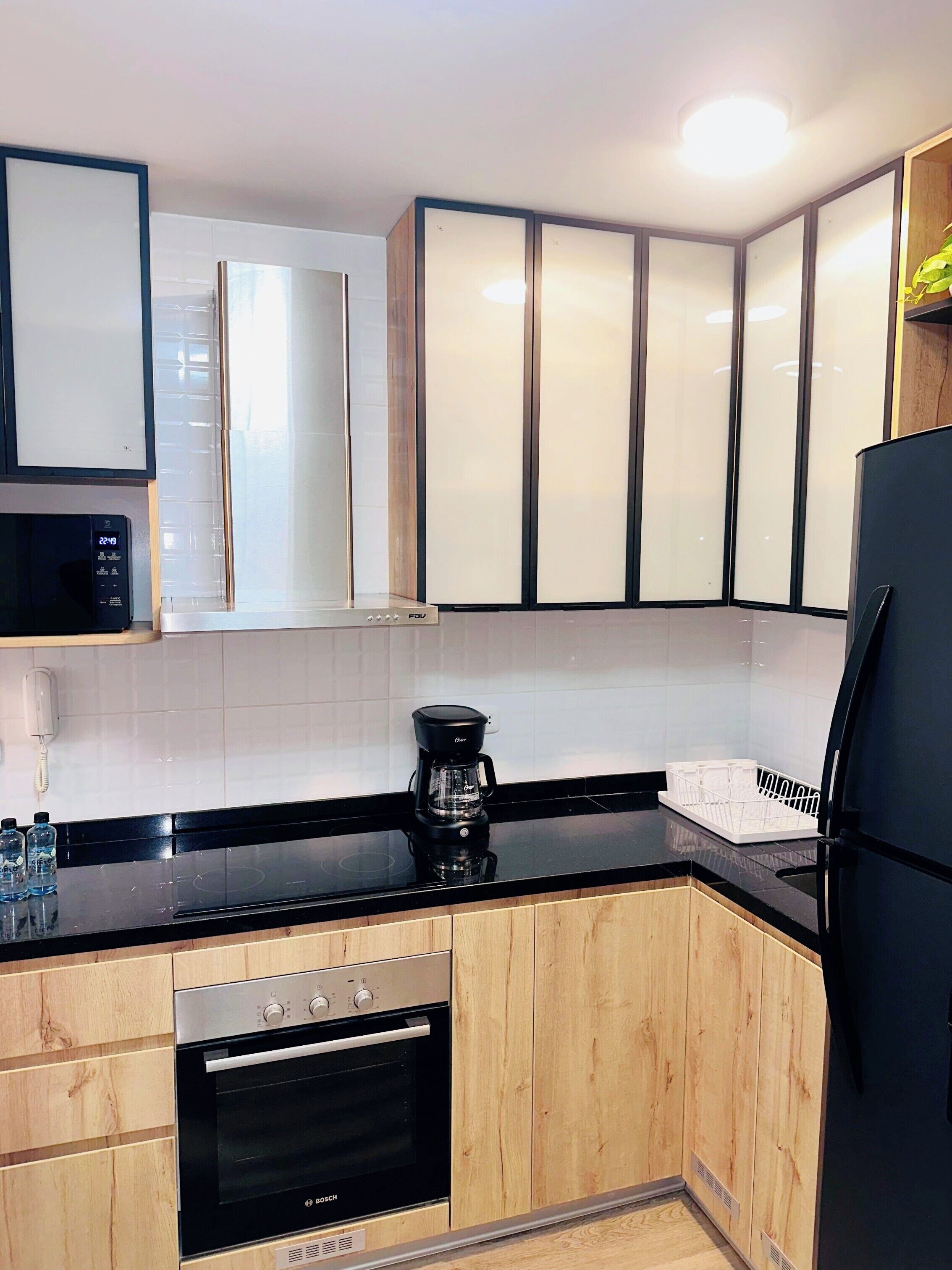 Eine moderne Küche mit Holzausstattung, einem Bosch-Backofen, einem schwarzen Kühlschrank und einer Kaffeemaschine auf der Arbeitsfläche.