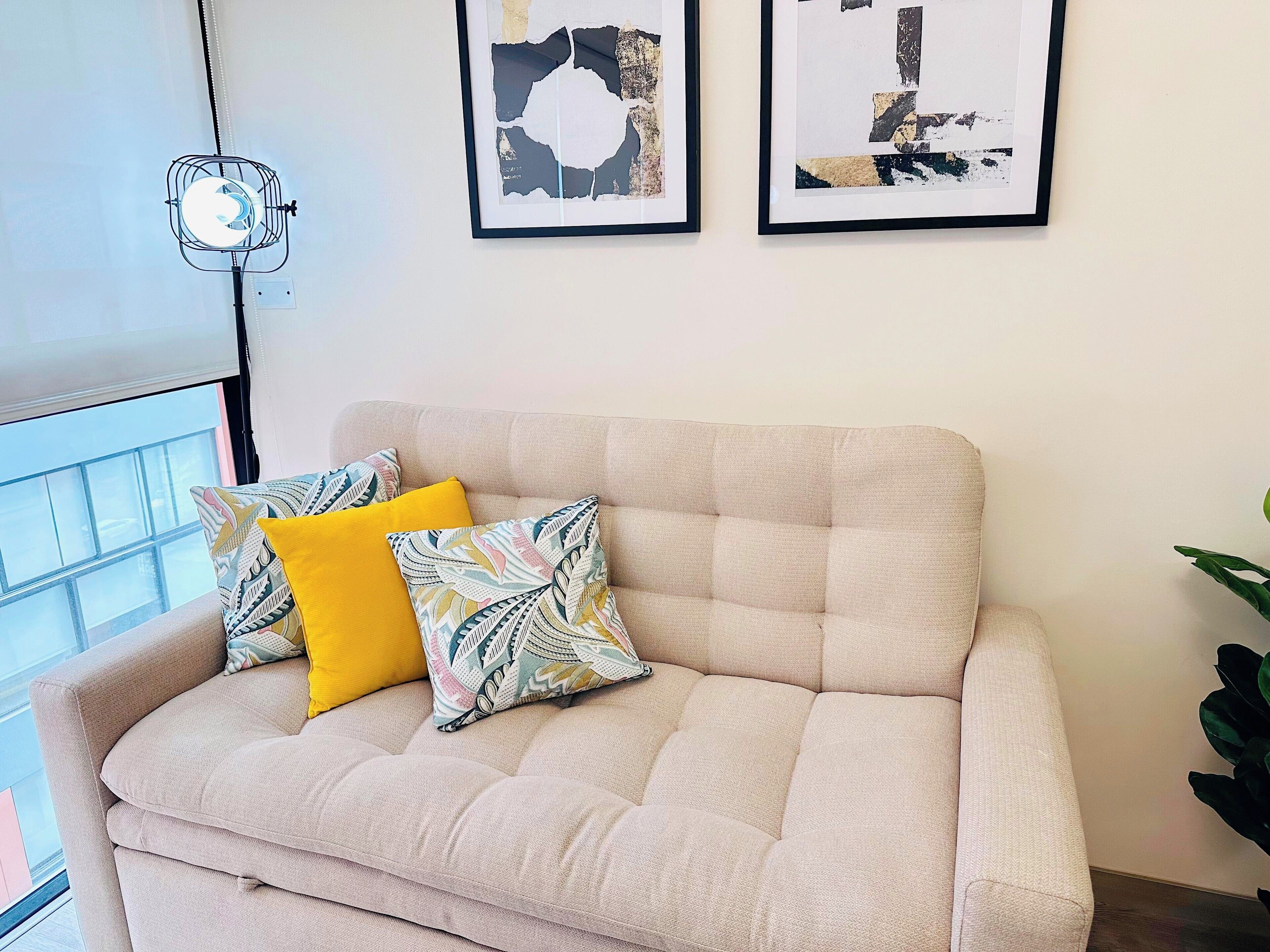 A beige sofa with patterned cushions, a wall-mounted fan, and abstract art.