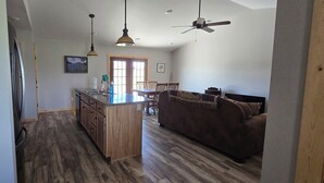 A spacious living area with a wooden floor, a kitchen island, a brown sofa, and a ceiling fan.