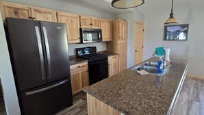 A kitchen with wooden cabinets, a black refrigerator, a microwave, a stove, and a sink with cleaning supplies.