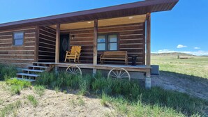 A log cabin with a porch, wooden rocking chairs, and a wagon wheel.