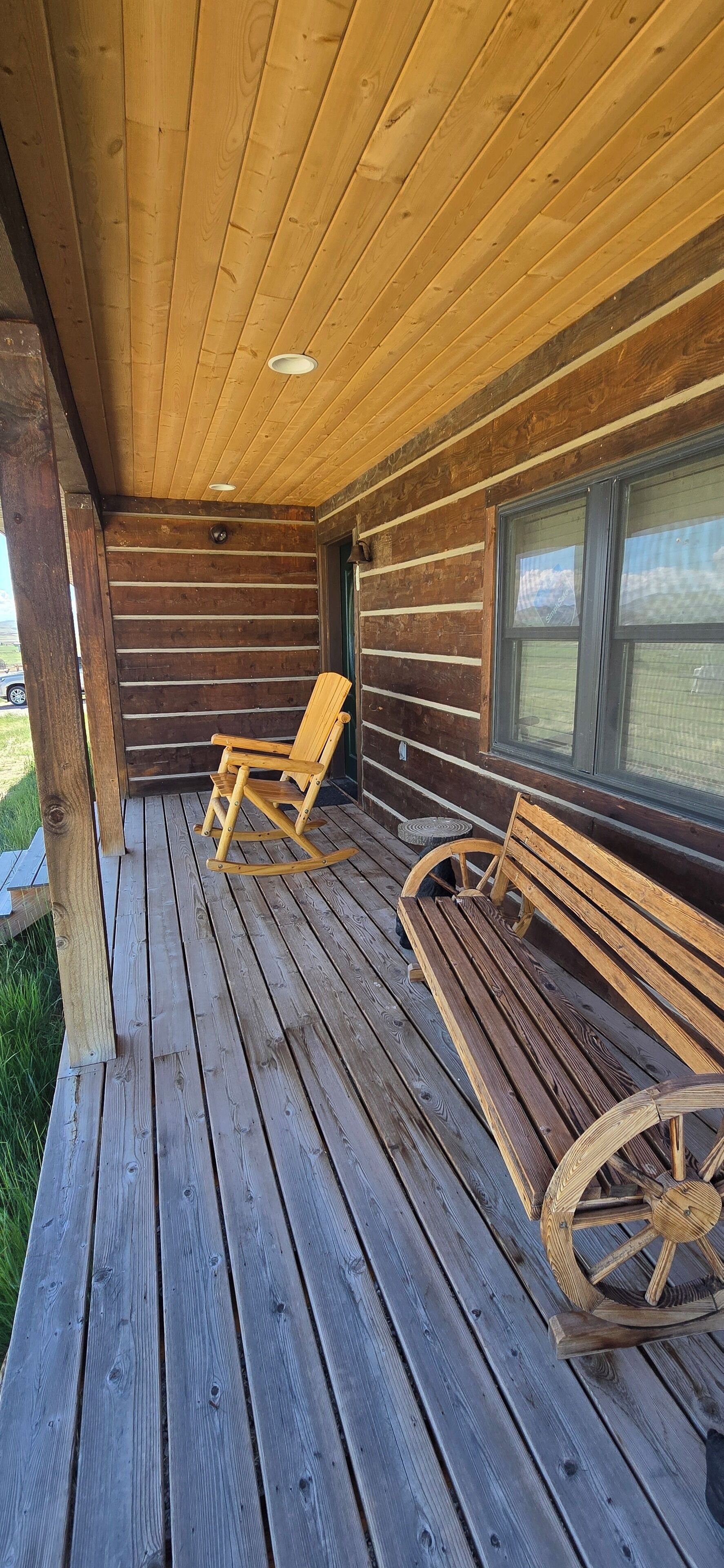 Een houten terras met twee schommelstoelen en een bank, een raam en een plafond met houten balken.