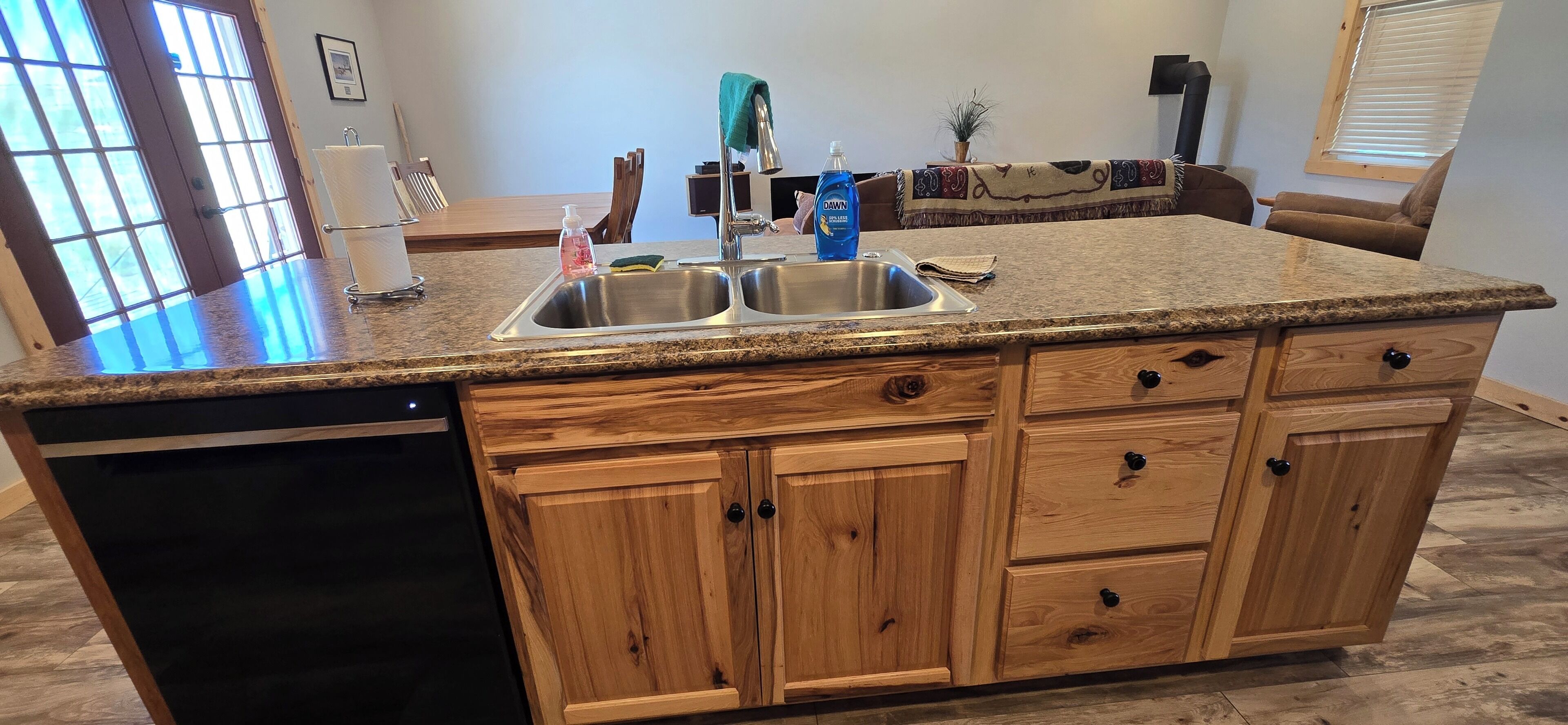 A kitchen with granite countertops, wooden cabinets, a dishwasher, and a window with blinds.